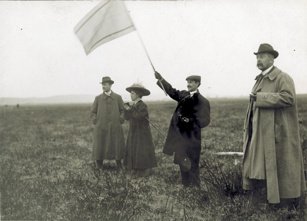 Orville Wright waves a signal flag as (from left Charles S. Rolls, Katharine Wright, and Dr. Speakman stand nearby, in France, 1909. (photo ms1_18_3_11)