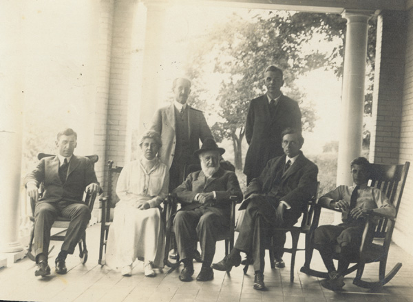 Group sitting and standing on the porch of the Wright Hawthorn Hill home, 1915. Left to right: Pliny Williamson, Katharine, Orville (standing), and Bishop Milton Wright, Earl N. Findley (standing), John R. McMahon, and Horace Wright. (photo ms1_26_5_5)